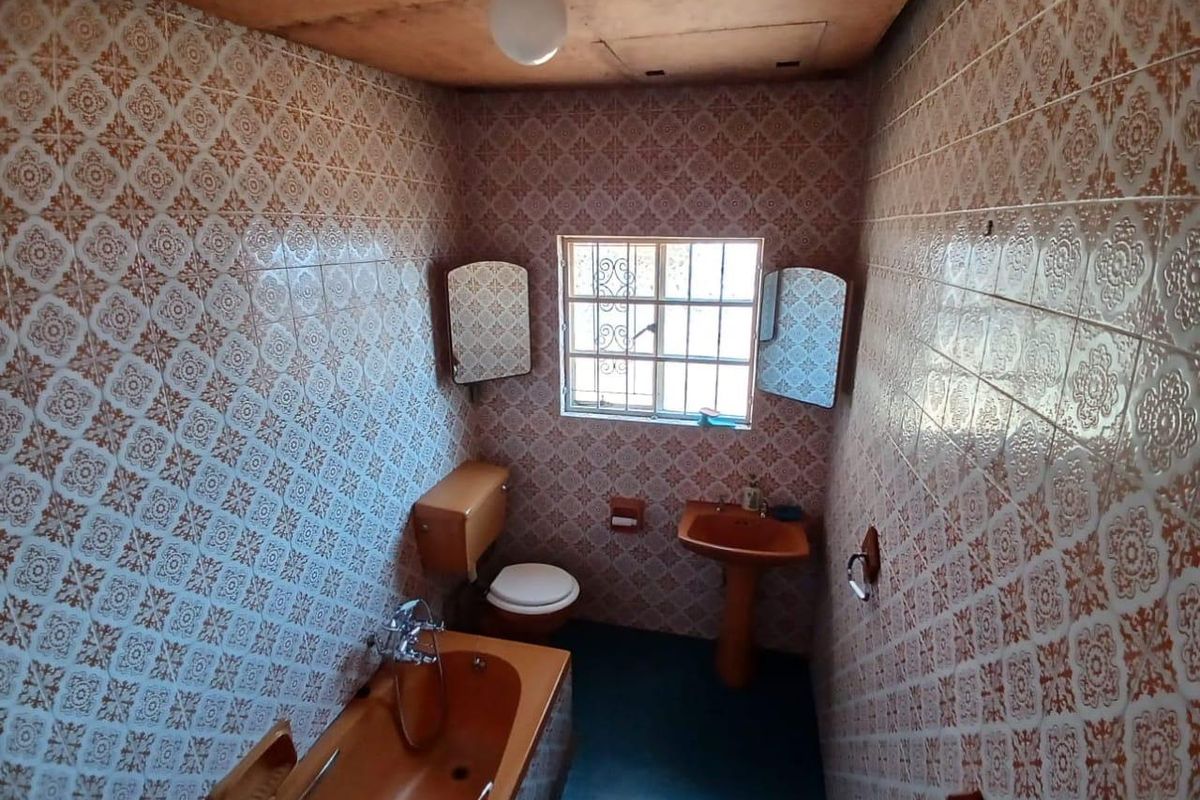 A dated bathroom featuring original patterned wall tiles, a pedestal basin, and a built-in bathtub with a shower mixer.