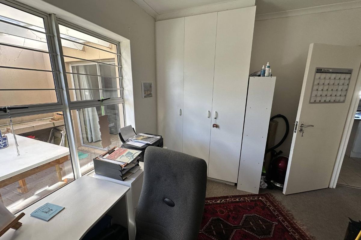 A functional bedroom featuring built-in cupboards, carpeted flooring, and large windows with security bars, offering natural light and practical storage space.
