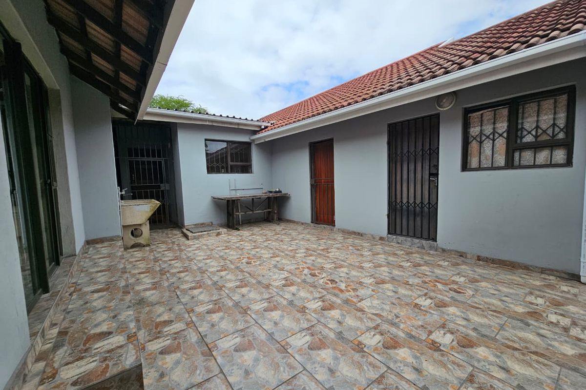 A paved rear courtyard area featuring a utility sink, multiple access doors with security gates, and tiled flooring.