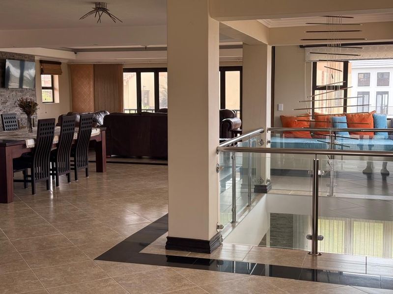 Spacious open-plan living and dining area featuring tiled floors, a stone feature wall, and a modern glass balustrade overlooking the lower level.