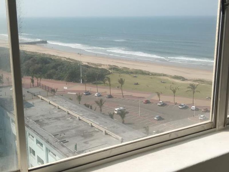 A clear elevated view of the coastline, beach, and promenade captured through an apartment window.