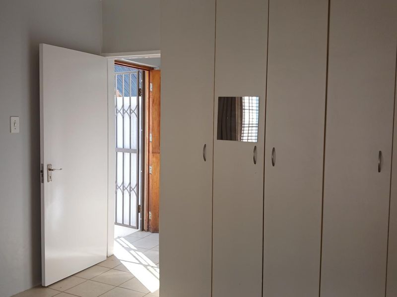 A clean, empty bedroom featuring built-in cupboards, tiled flooring, and a doorway leading to an exterior security gate.