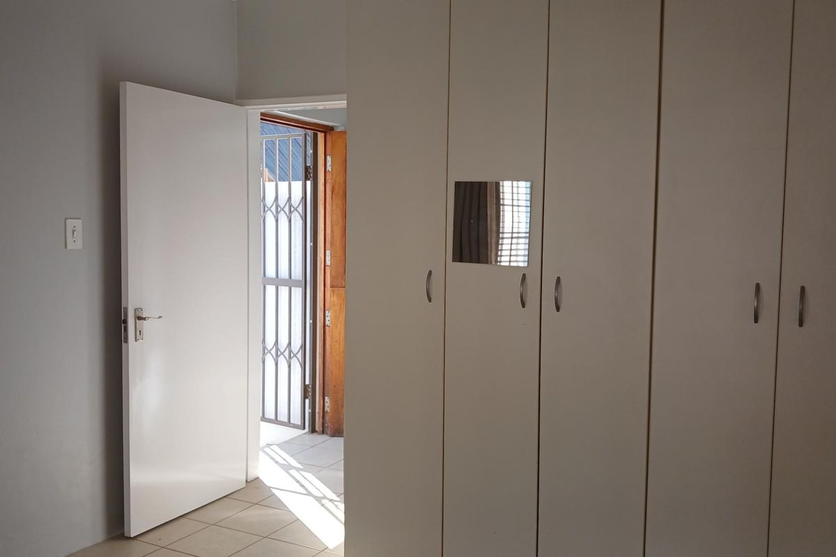 A clean, empty bedroom featuring built-in cupboards, tiled flooring, and a doorway leading to an exterior security gate.
