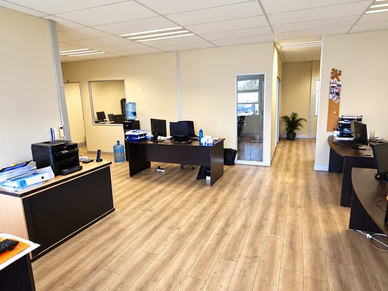 A spacious, well-lit open-plan office area featuring modern laminate flooring, a suspended ceiling with recessed lighting, and an integrated air conditioning unit.