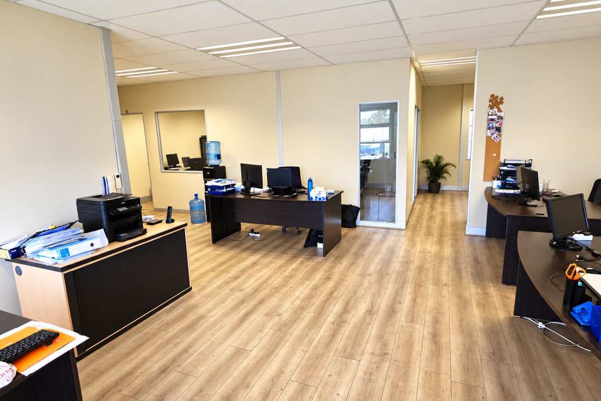 A spacious, well-lit open-plan office area featuring modern laminate flooring, a suspended ceiling with recessed lighting, and an integrated air conditioning unit.