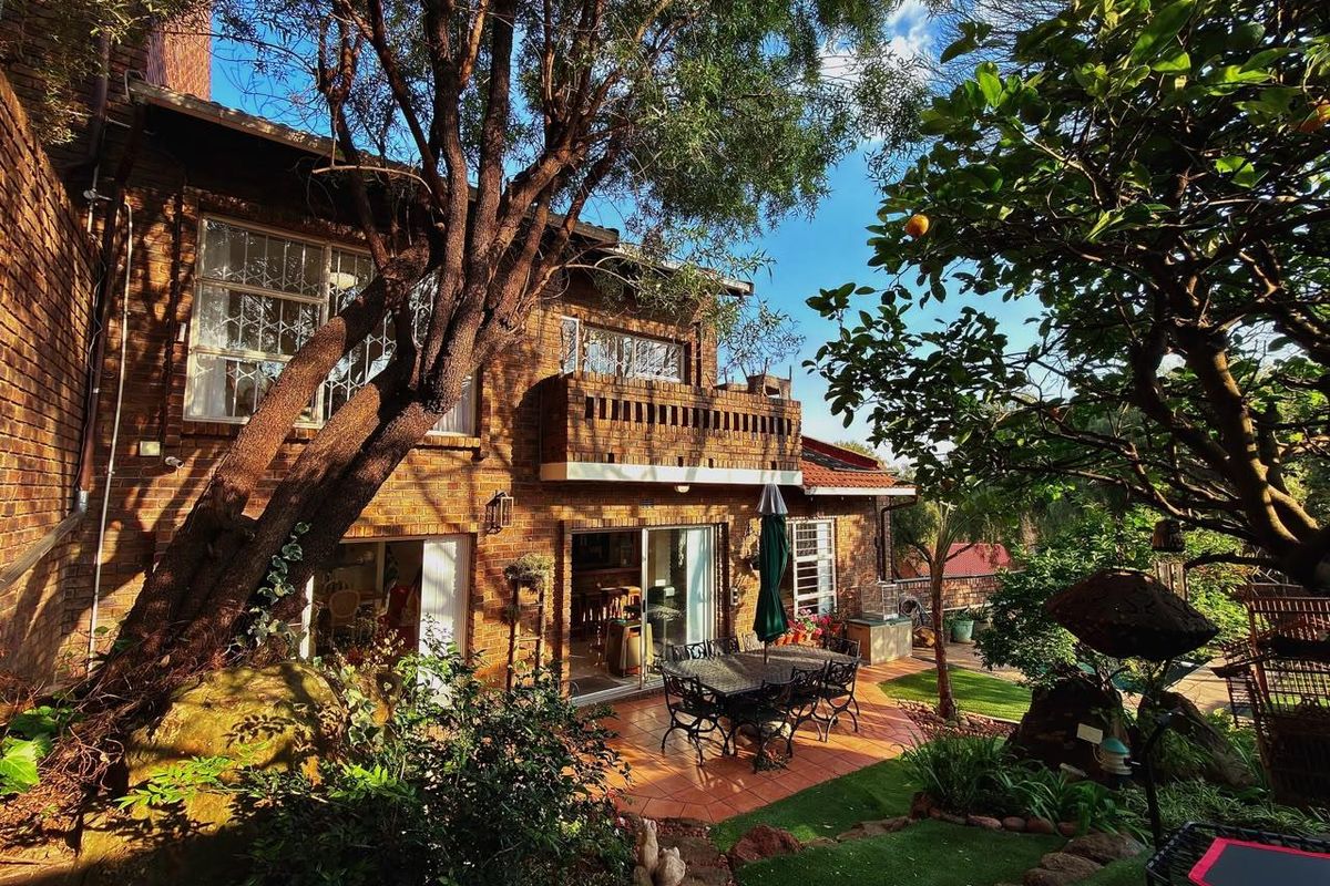 Rear view of a double-story brick townhouse featuring a tiled patio, balcony, and established garden setting.