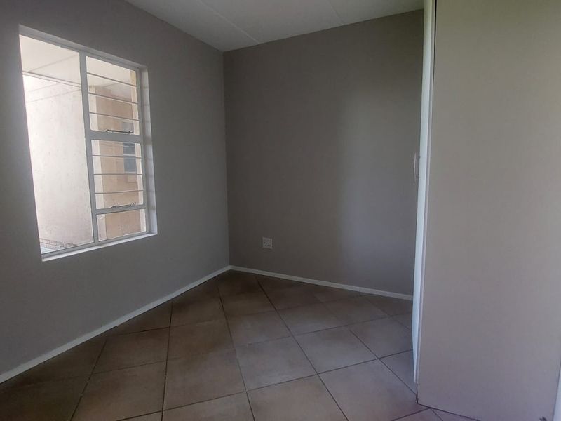 An empty bedroom featuring tiled flooring, a window with security bars, and a built-in cupboard, offering a neutral canvas for personalization.