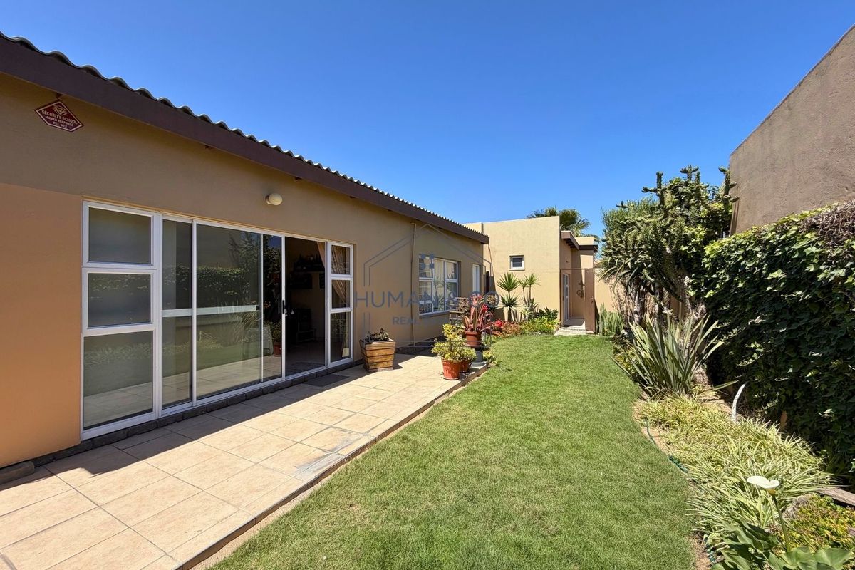 Rear exterior view featuring a tiled patio area, sliding glass doors, and a well-maintained lawn with established garden borders.