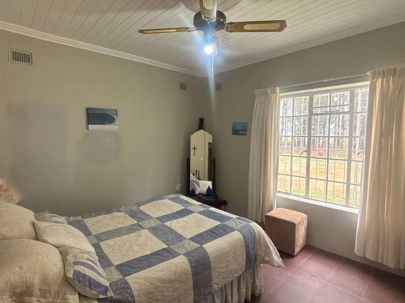 A bedroom featuring a ceiling fan, tiled flooring, and a large grid-pattern window allowing natural light.