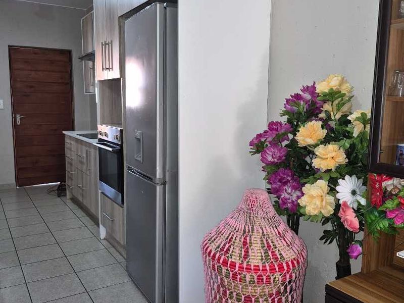 A functional kitchen featuring modern wood-finish cabinetry, built-in oven, extractor fan, and neutral tiled flooring, leading to a solid wood entrance door.