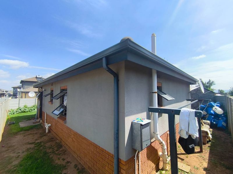 Rear exterior view of the property featuring plastered walls with a brick plinth, guttering system, and top-hung windows.