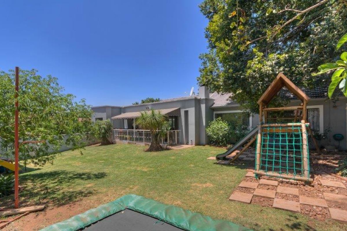 Rear view of the house featuring a lawn, mature trees, and a covered patio area with metal railings.