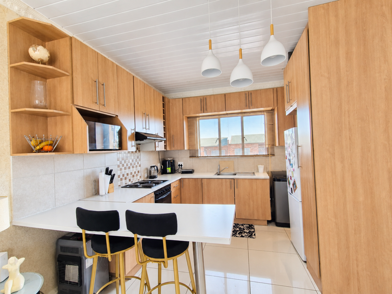 A well-maintained kitchen featuring light wood cabinetry, laminate countertops, a built-in hob with extractor fan, and a breakfast bar area.