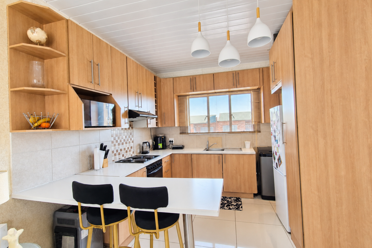 A well-maintained kitchen featuring light wood cabinetry, laminate countertops, a built-in hob with extractor fan, and a breakfast bar area.