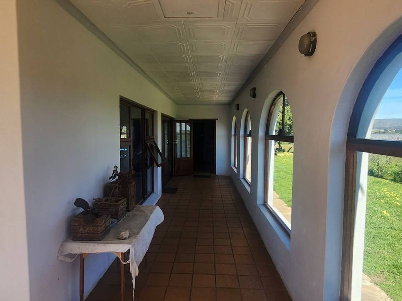 A covered patio featuring tiled flooring, arched windows with timber frames, and views overlooking the surrounding farm landscape.