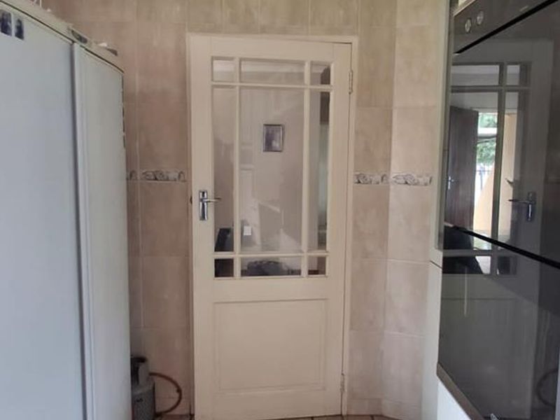 A functional kitchen area featuring built-in oven, tiled flooring, and a classic glass-panelled door leading to the adjacent space.