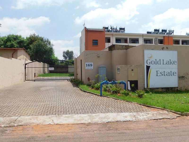 Front entrance view of Gold Lake Estate townhouse complex featuring a paved driveway, security gate, and perimeter wall with signage.