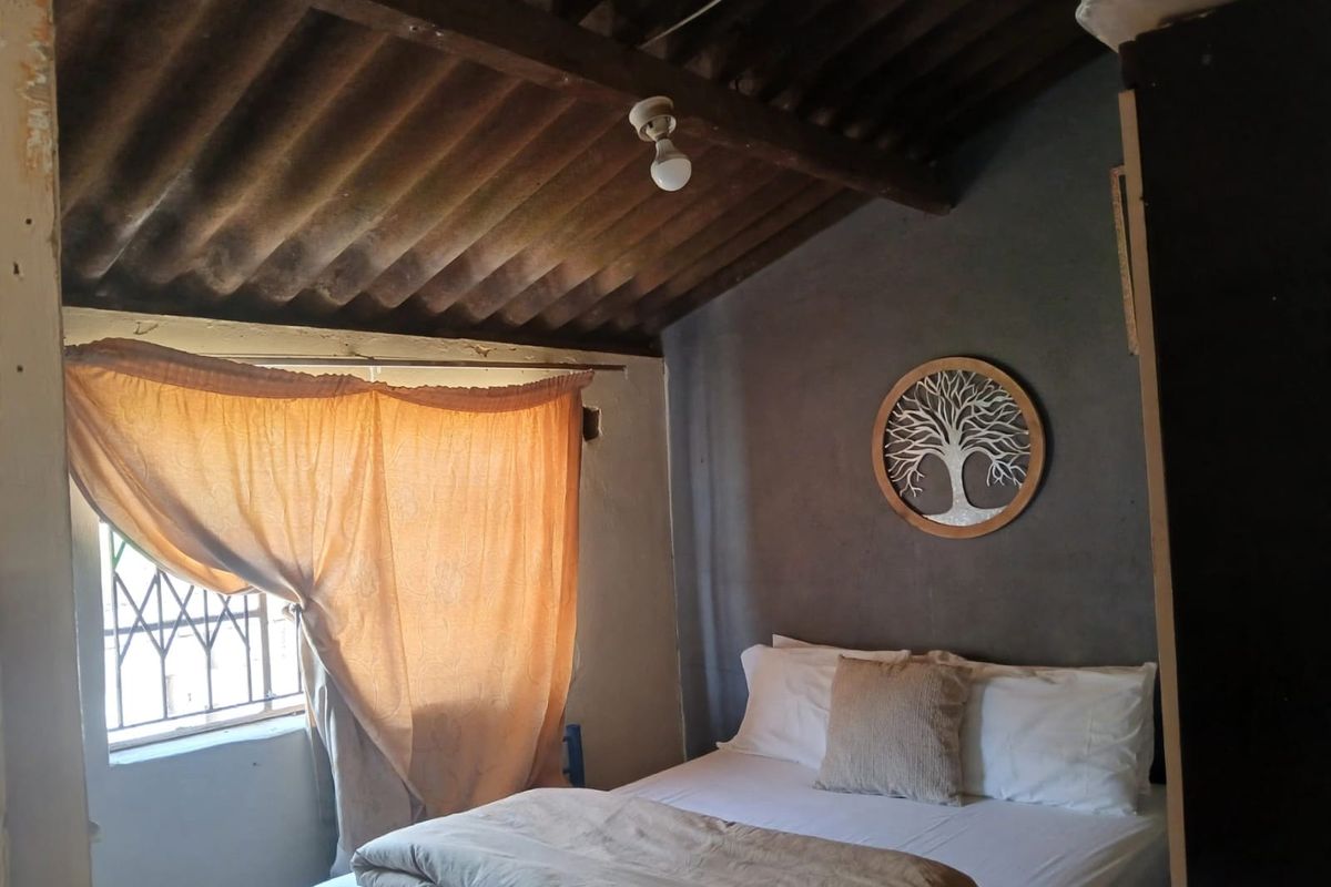 A bedroom featuring exposed timber rafters and corrugated roof sheeting, with security bars on the window and a dark feature wall.