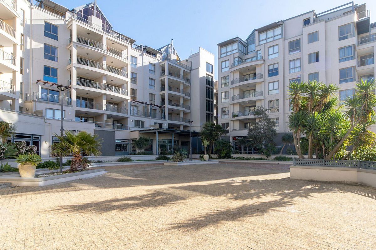 A spacious paved courtyard area situated between modern apartment blocks, featuring landscaped garden beds and multiple levels of private balconies.