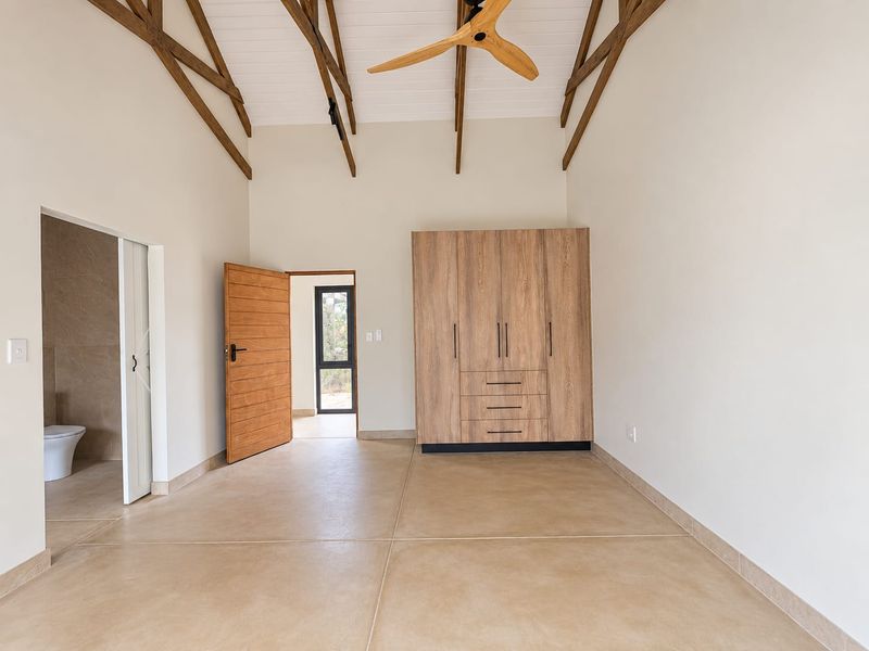 Spacious bedroom featuring vaulted ceilings with exposed timber trusses, built-in wardrobes, and direct access to an en-suite bathroom.