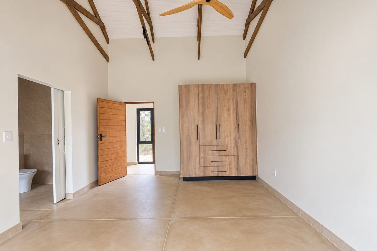 Spacious bedroom featuring vaulted ceilings with exposed timber trusses, built-in wardrobes, and direct access to an en-suite bathroom.