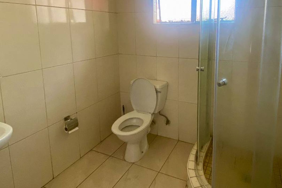 A functional bathroom featuring a corner shower enclosure with glass doors, a standard toilet, and full-height wall tiling.