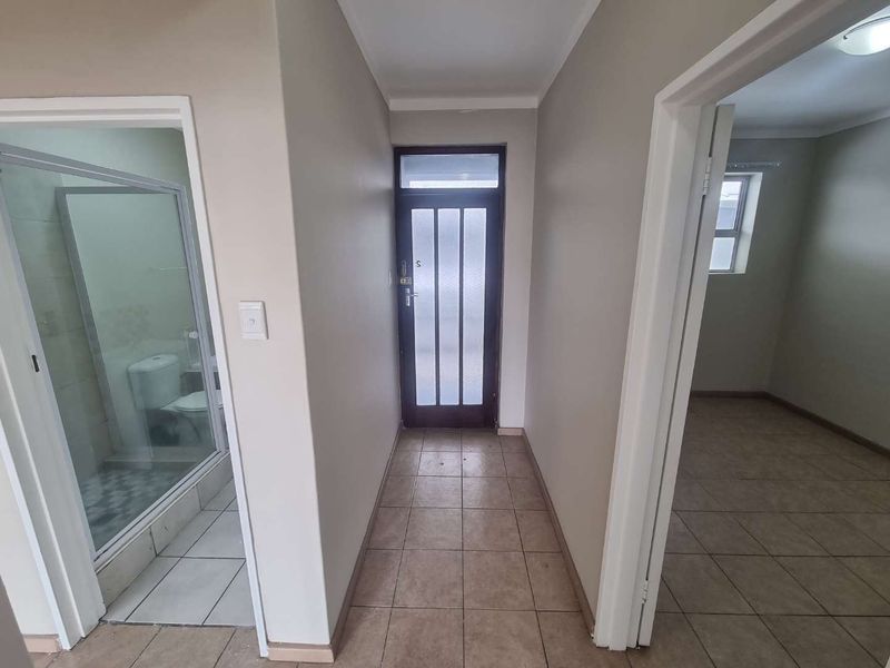 A clean, neutral-toned hallway featuring tiled flooring and a glass-paneled entrance door, providing access to adjacent rooms.