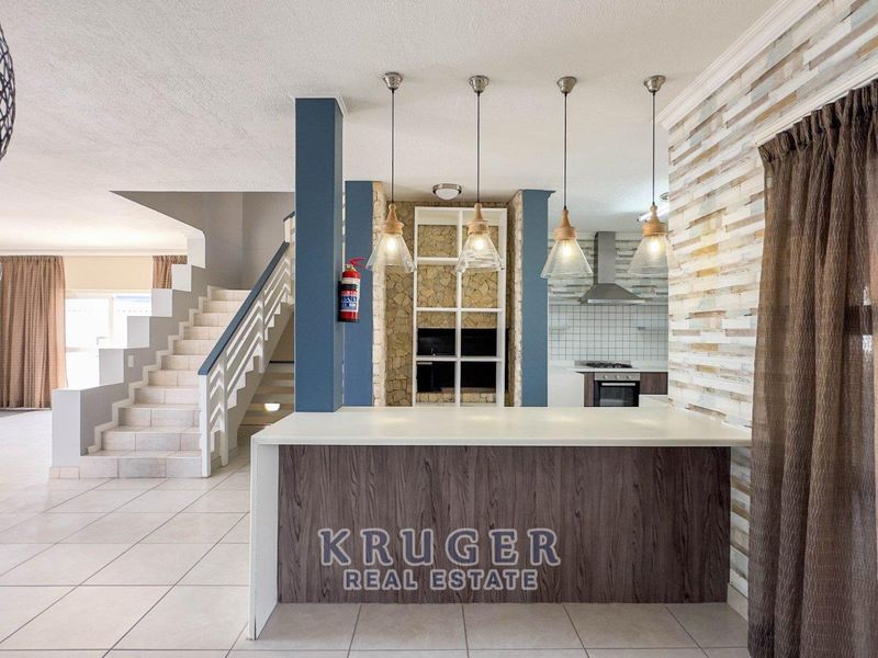 Open plan living area featuring a modern kitchen island, stone accent wall, and a central staircase with tiled flooring throughout.