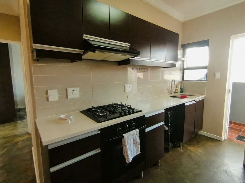 A functional kitchen featuring dark cabinetry, stone countertops, a gas hob, built-in oven, extractor fan, and a stainless steel sink with tiled backsplash.