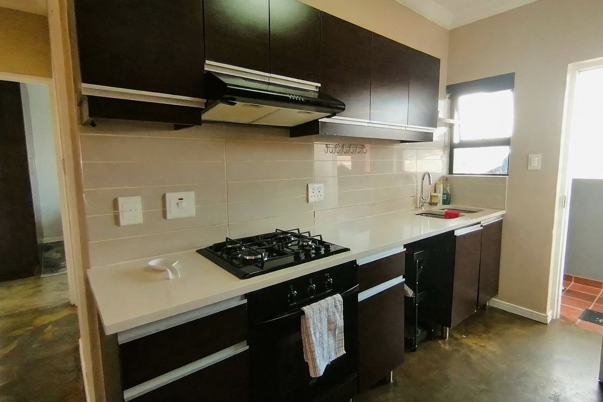 A functional kitchen featuring dark cabinetry, stone countertops, a gas hob, built-in oven, extractor fan, and a stainless steel sink with tiled backsplash.
