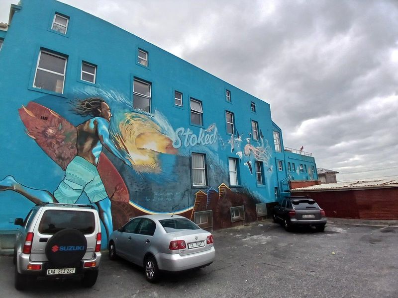 Rear exterior view of the apartment building featuring a large decorative mural and an adjacent asphalt parking area.