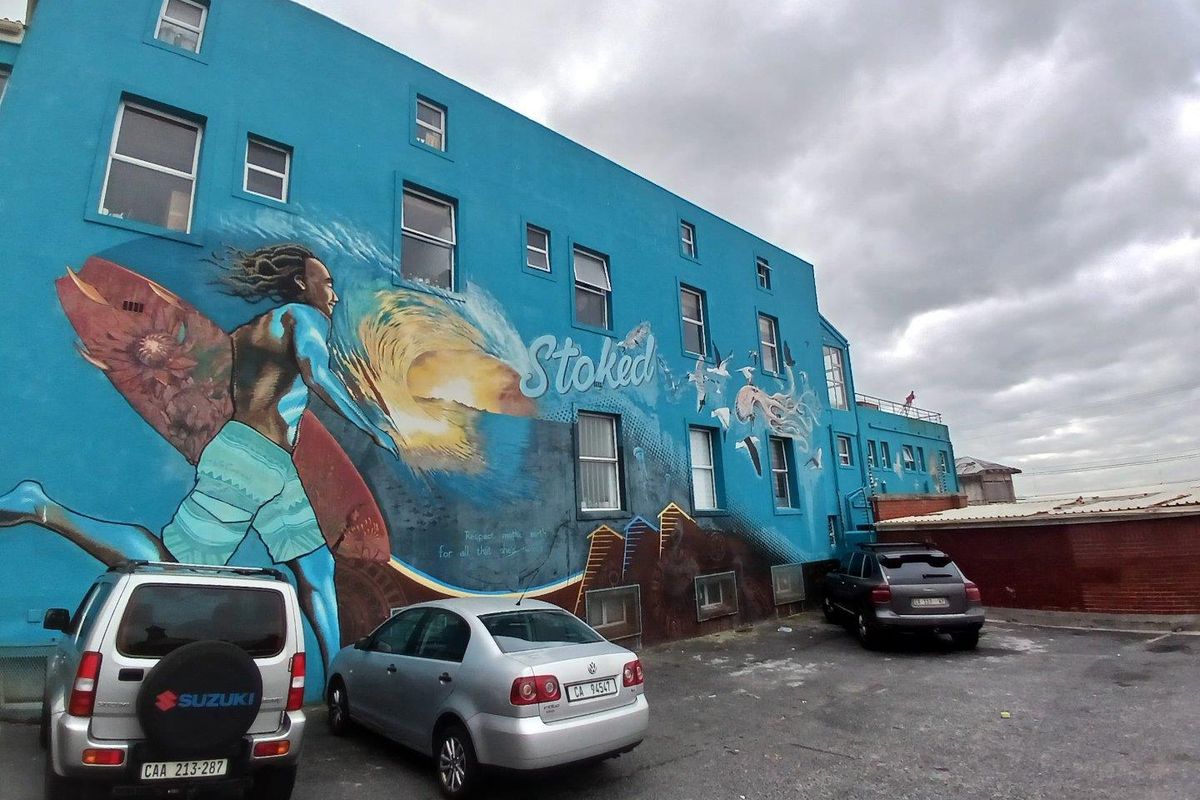 Rear exterior view of the apartment building featuring a large decorative mural and an adjacent asphalt parking area.