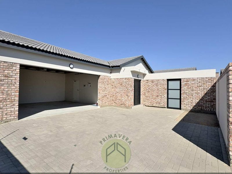 A well-maintained front exterior view featuring a spacious paved driveway, double garage, and attractive face-brick detailing under a modern tiled roof.