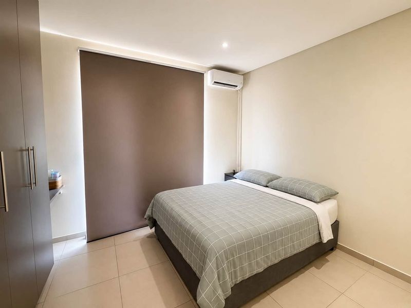 A modern, well-maintained bedroom featuring tiled flooring, a built-in wardrobe, and a wall-mounted split-system air conditioner.