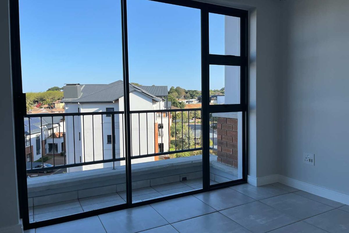 Bright living area featuring large sliding glass doors that open onto a private balcony with neighbourhood views and modern tiled flooring.