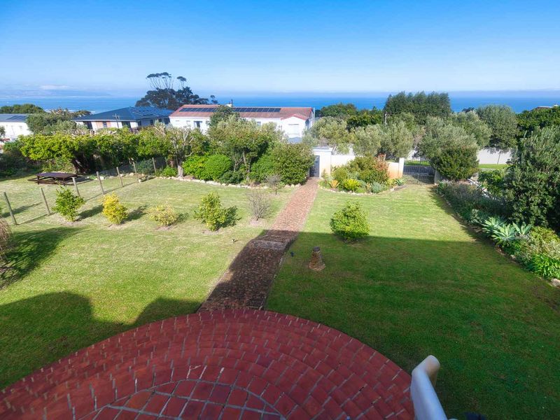 A spacious, well-maintained garden featuring a brick pathway, lush lawn, and mature landscaping, offering a pleasant outdoor space with distant ocean views.