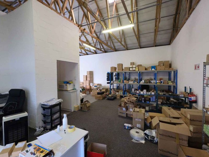 Industrial utility space featuring exposed timber roof trusses, painted concrete block walls, and functional industrial shelving units for storage.