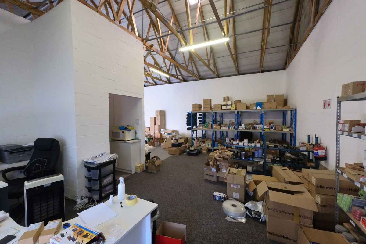 Industrial utility space featuring exposed timber roof trusses, painted concrete block walls, and functional industrial shelving units for storage.