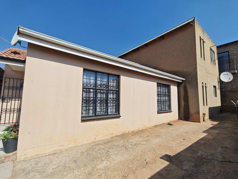 Rear exterior view of the property featuring plastered walls, security bars on windows, and an unpaved ground area.