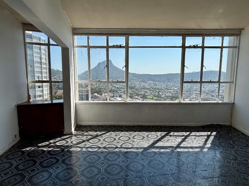 An empty living room featuring expansive windows with panoramic mountain and city views, offering a blank canvas for renovation and modernization.