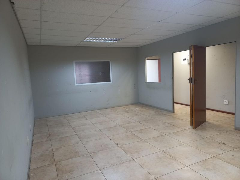 An empty office space featuring ceramic floor tiles, a suspended ceiling with recessed lighting, and an internal window connecting to an adjacent room.