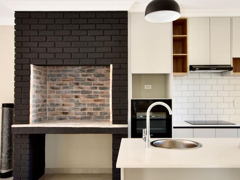 Modern kitchen featuring a striking black brick fireplace, sleek cabinetry, subway tile backsplash, and a central island with an integrated sink.