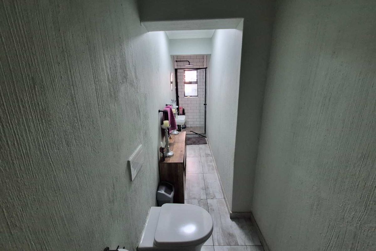 A narrow bathroom featuring a wall-mounted toilet, tiled flooring, and a walk-in shower enclosure with tiled walls.