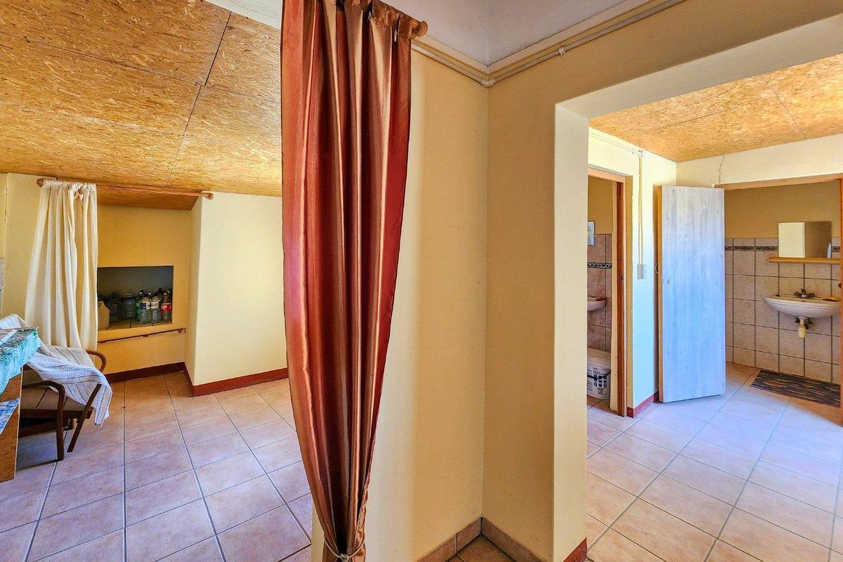Interior view showing a bedroom area with tiled flooring, wood-panelled ceiling, and an adjacent bathroom with basic sanitary fixtures.