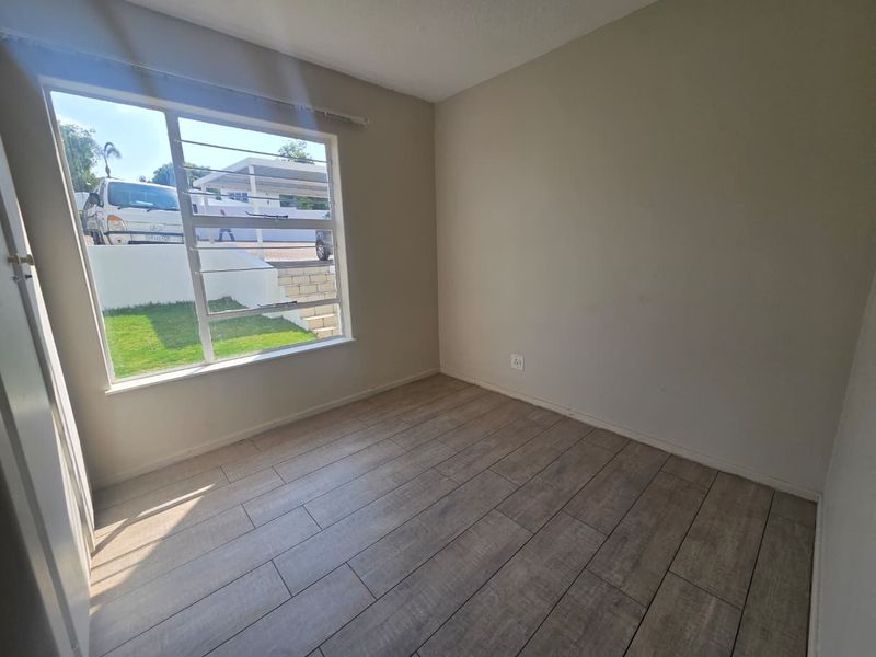 A bright, empty bedroom featuring modern wood-look laminate flooring and a large window with security bars, offering a clean and neutral living space.