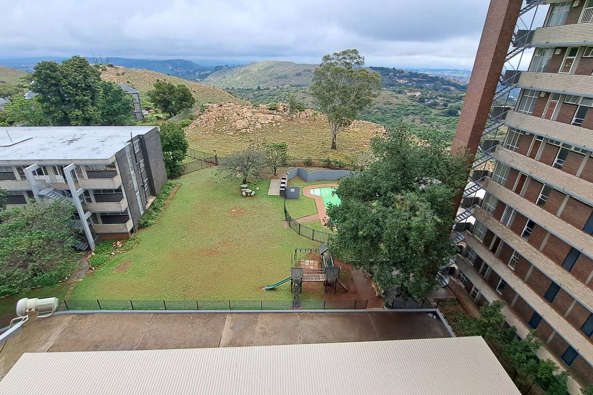 Elevated aerial view overlooking the apartment complex grounds, featuring a communal garden, swimming pool area, and scenic hillside landscape.
