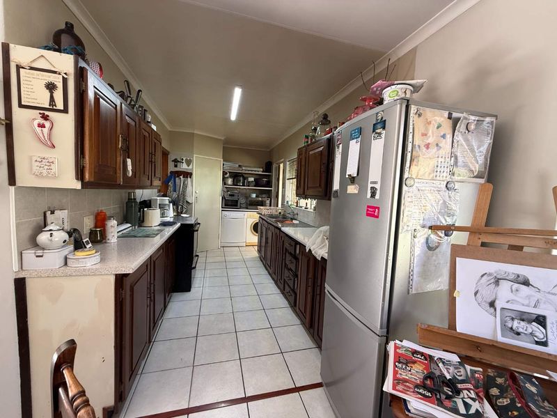 Galley-style kitchen featuring timber cabinetry, laminate countertops, and ceramic floor tiles, offering a functional layout with integrated laundry space at the rear.