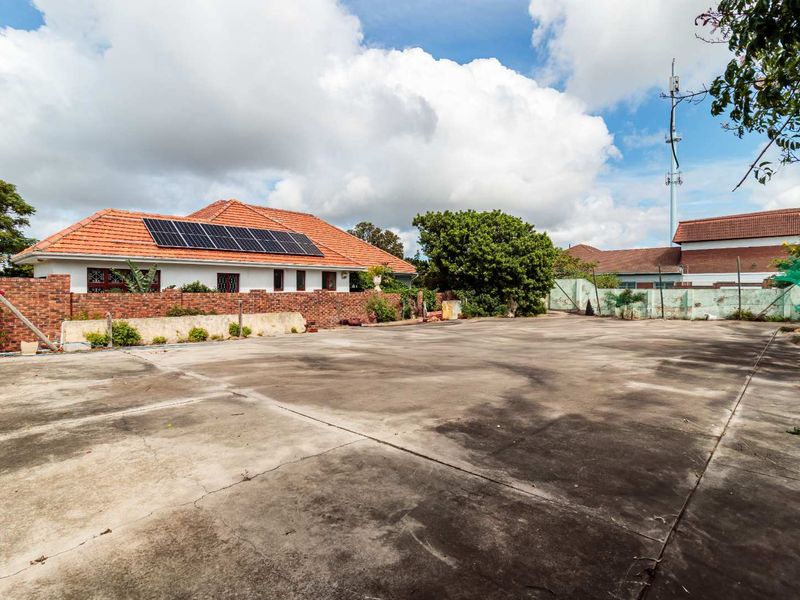 A spacious concrete paved area featuring a brick boundary wall and a residential building with roof-mounted solar panels.