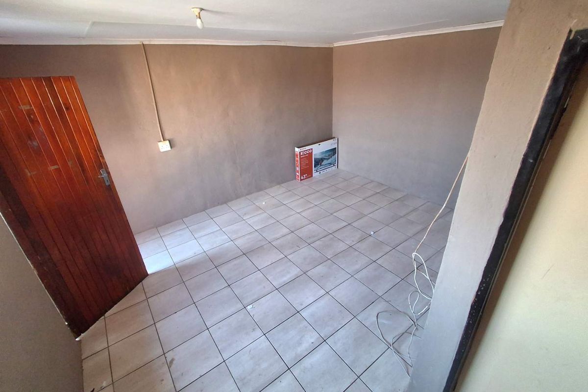 An empty bedroom featuring tiled flooring and a timber door, requiring cosmetic updates to the wall finishes and electrical fixtures.