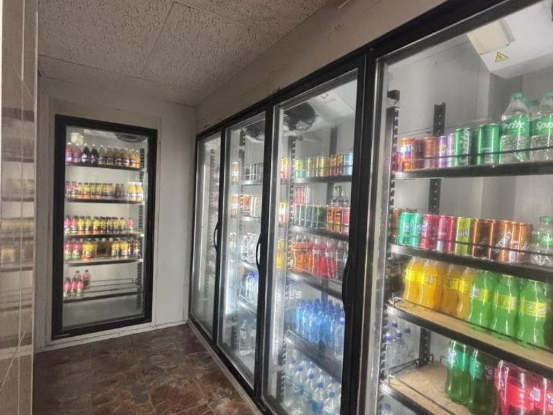 A utility area featuring multiple built-in commercial glass-door refrigeration units for beverage storage, finished with tiled flooring and a textured ceiling.